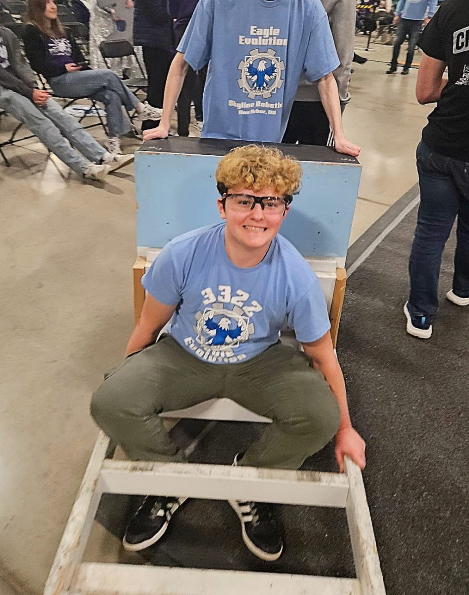 Grey Butka getting pushed around in a robot kart at robotics competition.