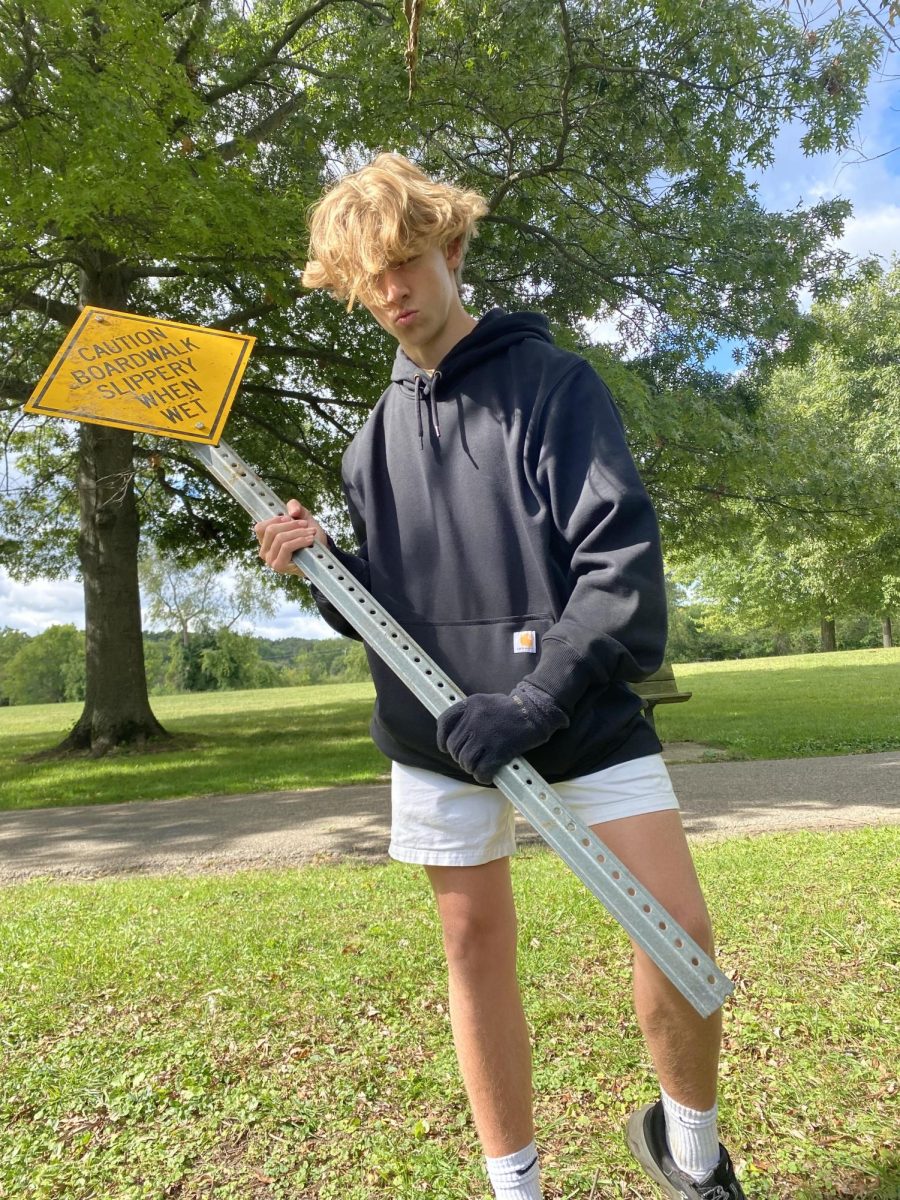 Reid Lobdell ('29) posing with a boardwalk sign while picking up trash with the Skyline Crew team.