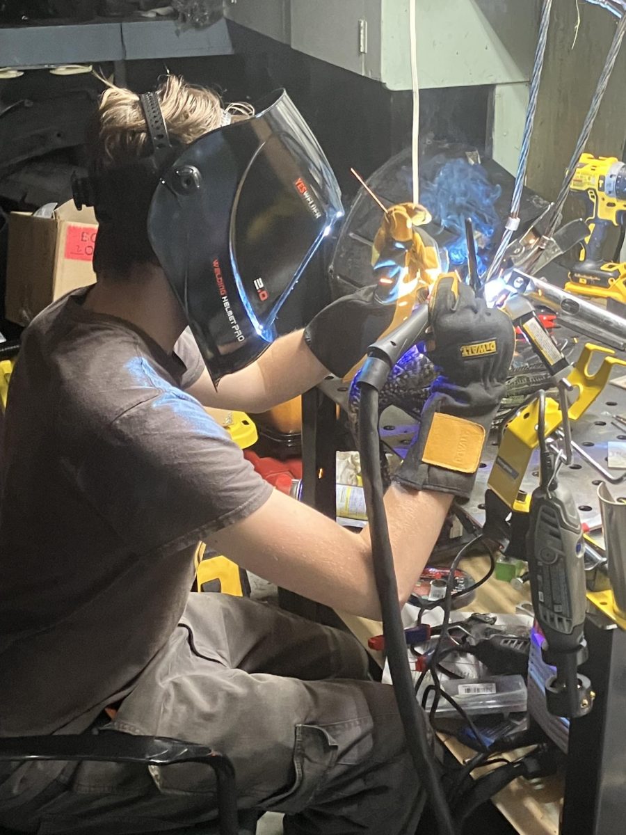 Spyder Cooney ('28) welding a metal sculpture.